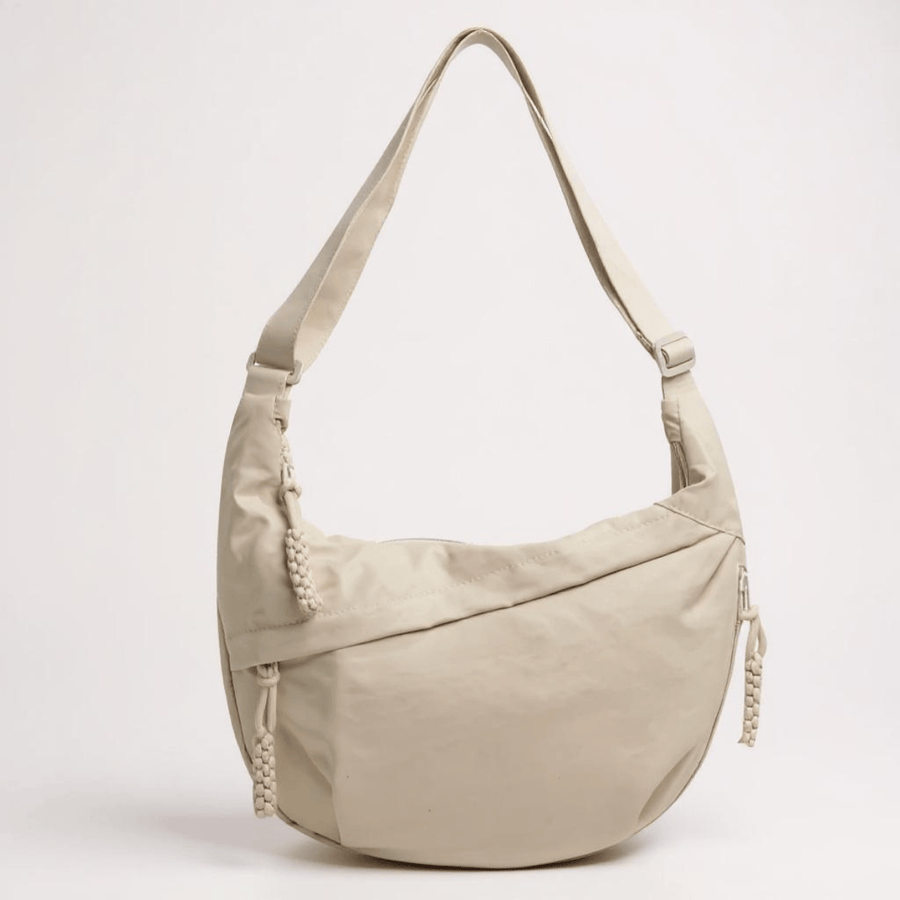 Beige crossbody bag by THE WHITMORE FAMILY named Elena, featuring a sleek design and adjustable strap, shown on a neutral background.