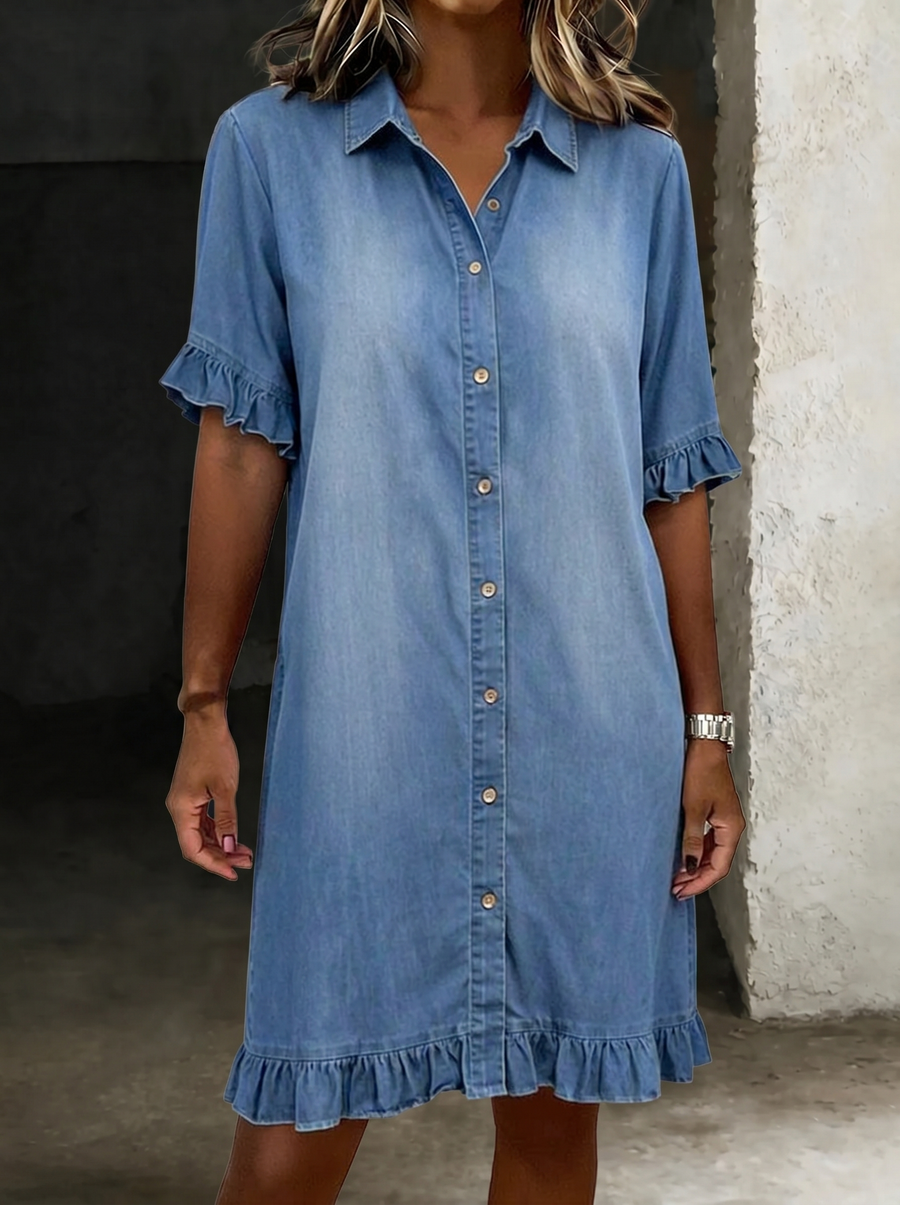 Maria denim dress by THE WHITMORE FAMILY featuring comfortable fabric and flattering pleats, shown on a hanger.