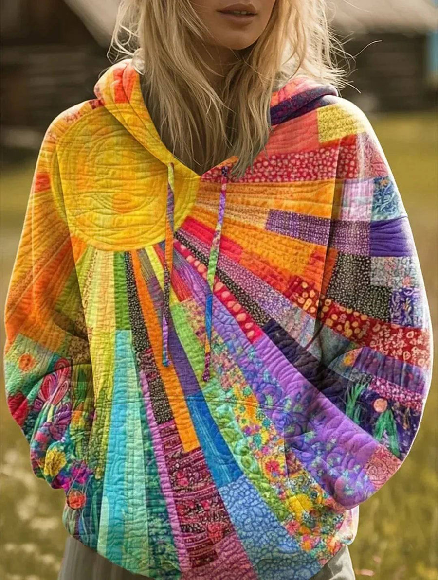The Alma Sunburst Hoodie by THE WHITMORE FAMILY, a cozy sweater with sunburst design in vibrant colors, displayed on a hanger.