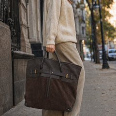 The Juliette Suede Tote bag by THE WHITMORE FAMILY, featuring a stylish tan suede exterior and spacious interior, held by a person.