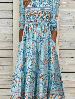 Blue Aphra Petal Muse Dress by THE WHITMORE FAMILY, displayed on a hanger with floral petal details and elegant fabric.