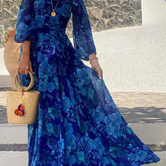 Blue Francesca long dress with floral print by THE WHITMORE FAMILY, featuring a flowing silhouette and vibrant flower patterns.