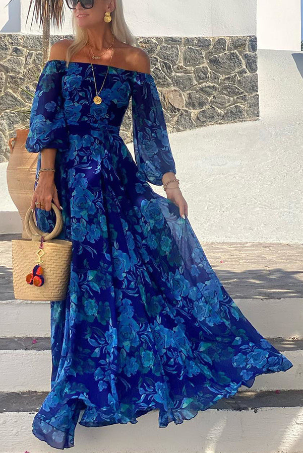 Blue Francesca long dress with floral print by THE WHITMORE FAMILY, featuring a flowing silhouette and vibrant flower patterns.