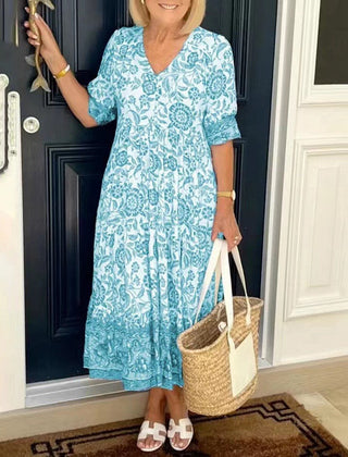 Blue Keisha floral V-neck dress by THE WHITMORE FAMILY, featuring a graceful design and vibrant floral pattern.