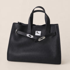 Black leather tote bag with sleek design from THE WHITMORE FAMILY, featuring sturdy handles and spacious interior.
