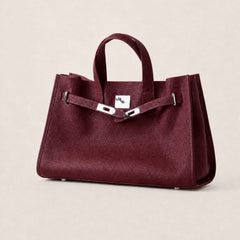 Maroon leather tote bag by THE WHITMORE FAMILY, featuring sturdy handles and sleek design, on a neutral background.