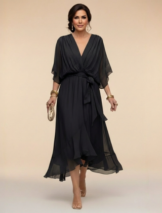 Green Sarah Sandra chiffon V-neck dress by THE WHITMORE FAMILY, displayed on a hanger with flowing fabric and elegant design.