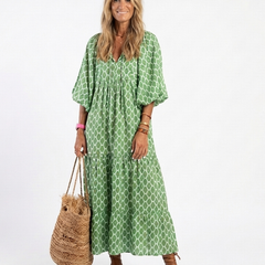 A woman wearing the Apolline three-quarter sleeve V-neck patterned midi dress by THE WHITMORE FAMILY, showcasing its stylish design.