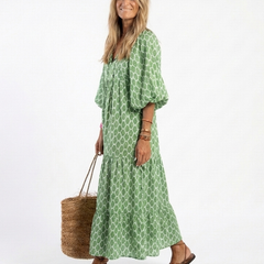 A woman wearing the Apolline three-quarter sleeve V-neck patterned midi dress by THE WHITMORE FAMILY, standing outdoors.