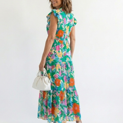 Lila floral V-neck tiered midi dress by THE WHITMORE FAMILY, showing the flowing fabric and vibrant floral pattern.