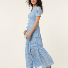 Brielle V neck short sleeve tiered midi dress by THE WHITMORE FAMILY, displayed on a hanger with a floral background.