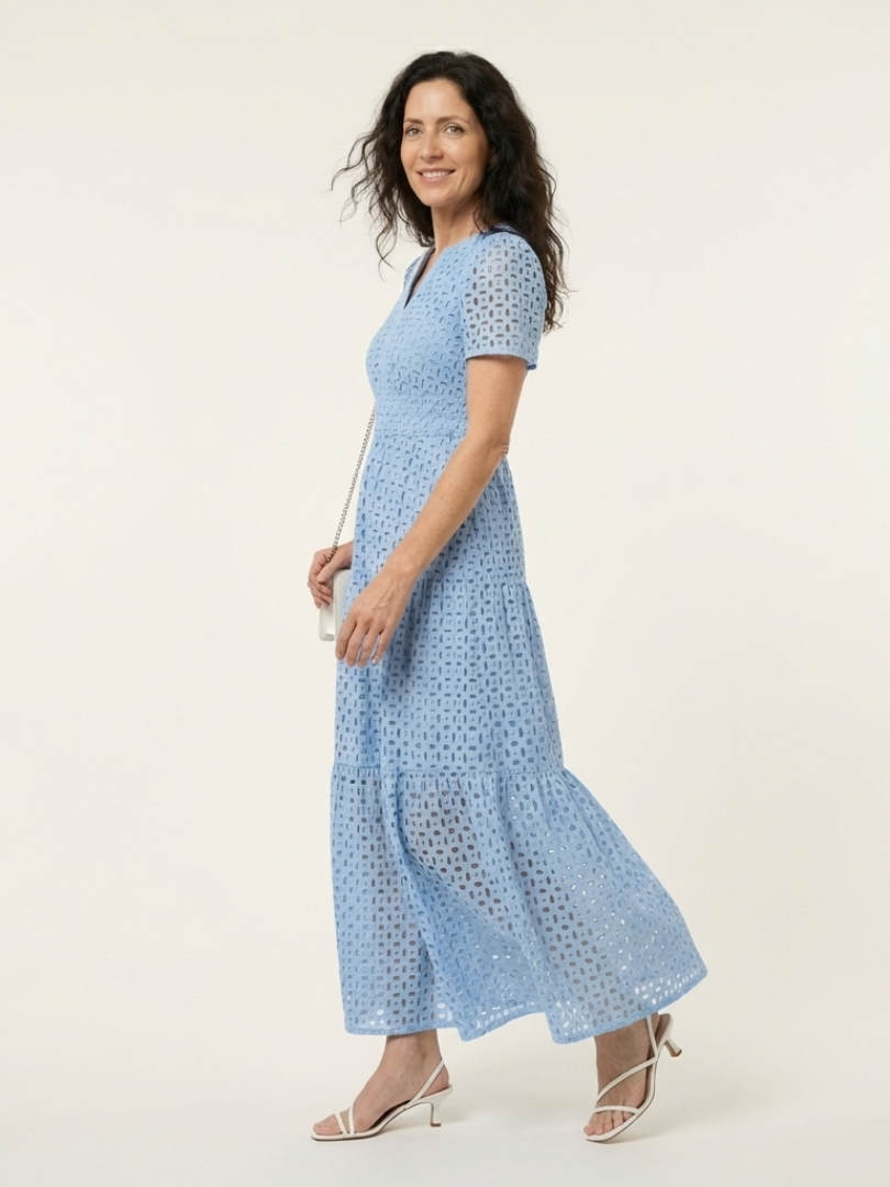 Brielle V neck short sleeve tiered midi dress by THE WHITMORE FAMILY, displayed on a hanger with a floral background.