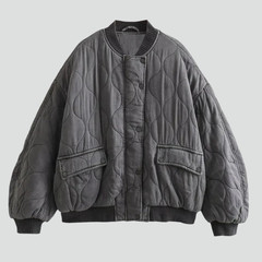 Women’s grey bomber jacket by THE WHITMORE FAMILY with snap closure and quilted surface, shown on a model.