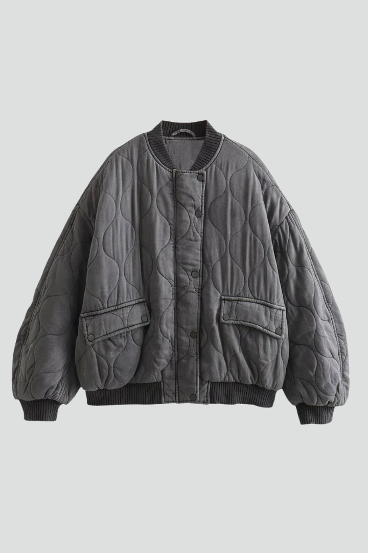 Women’s grey bomber jacket by THE WHITMORE FAMILY with snap closure and quilted surface, shown on a model.