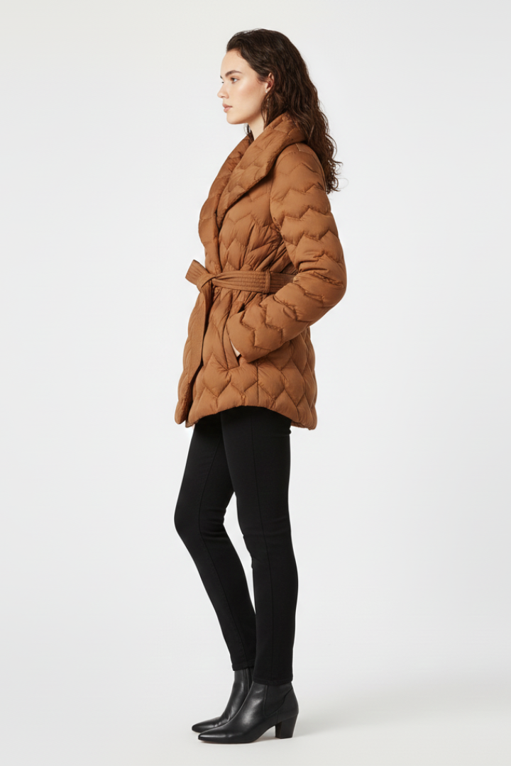 Women’s down coat by THE WHITMORE FAMILY in caramel, with belted waist and deep pockets, shown on a model.