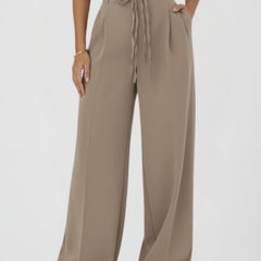 Women's wide-leg trousers with tie waist and high rise, by THE WHITMORE FAMILY, shown hanging on a clothing rack.