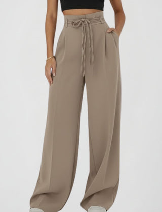 Women's wide-leg trousers with tie waist and high rise, by THE WHITMORE FAMILY, shown hanging on a clothing rack.