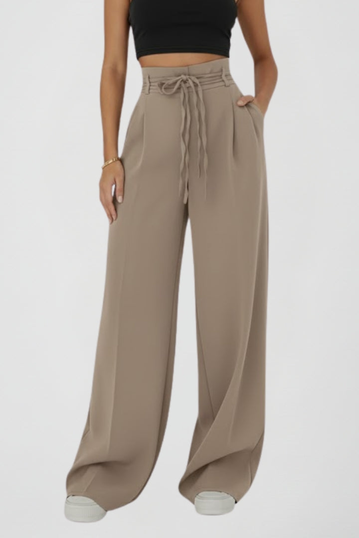 Women's wide-leg trousers with tie waist and high rise, by THE WHITMORE FAMILY, shown hanging on a clothing rack.