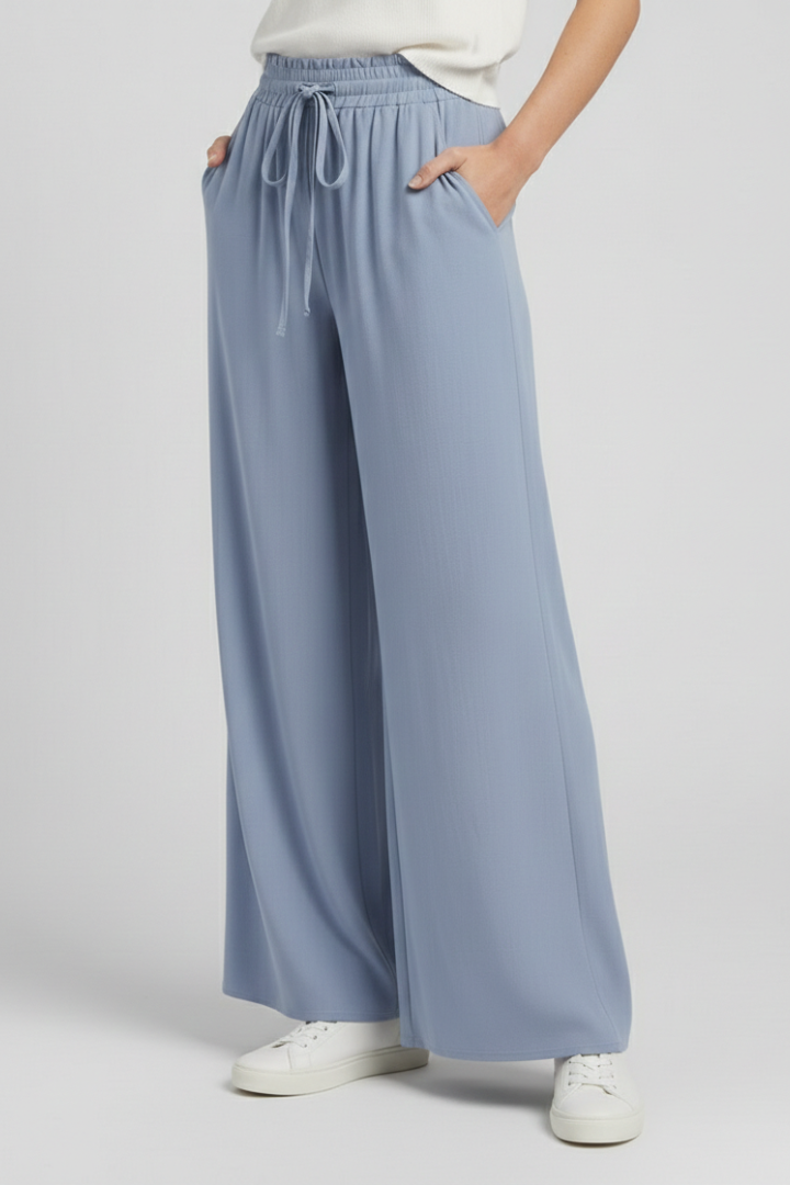 Light blue women’s palazzo trousers by THE WHITMORE FAMILY with drawstring waist and side pockets, relaxed and stylish fit.