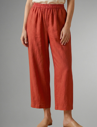 Women’s pink trousers with elastic waistband and wide legs by THE WHITMORE FAMILY, shown hanging on a hanger.